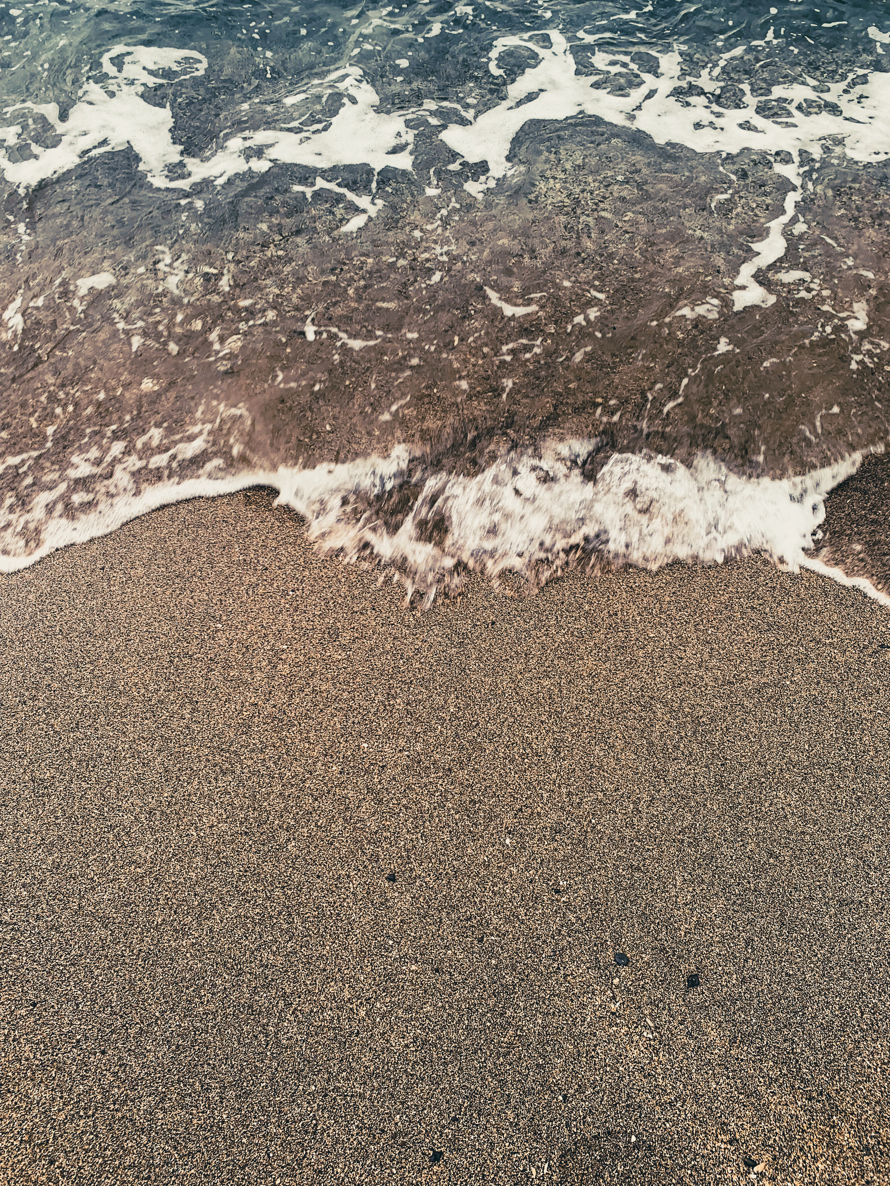 photo of turquoie green water washing up onto tan speckled sand at the beach, with a small white wave coming in, caught blurry by the camera.