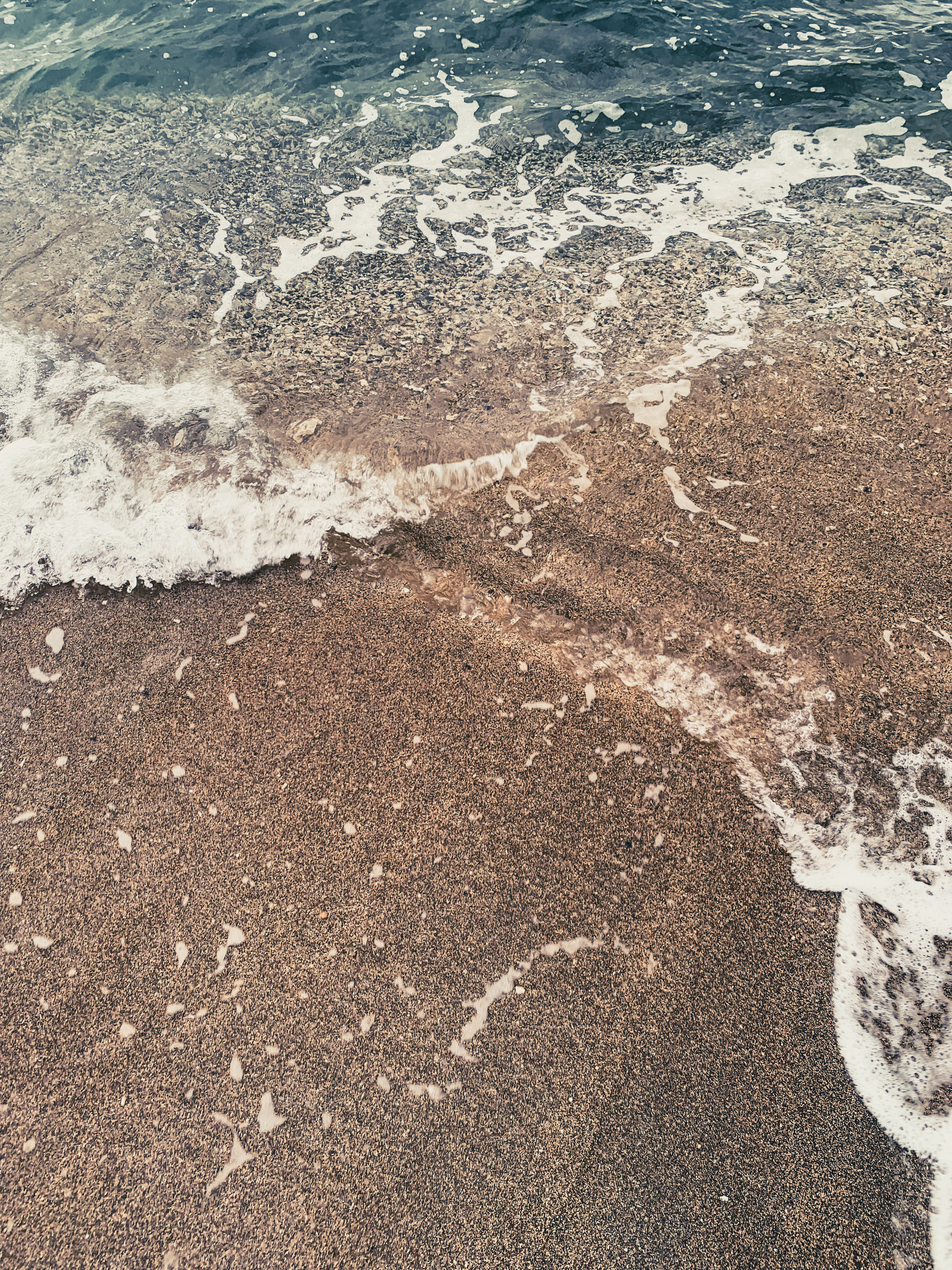 photo of somewhat blurry water on the beach, turquoise greenish water at the top washing in a clear ripple over brown and grey fine-grained sand, with some frothy edges, apparently moving across the sand.