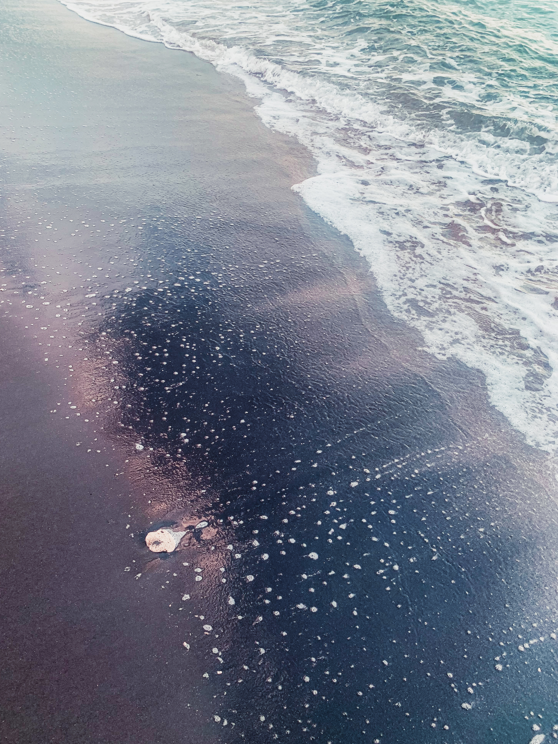 photo at the beach taken of the sand with a wave recently washed over it and spotty froth in a sheer glossy layer over the ooze