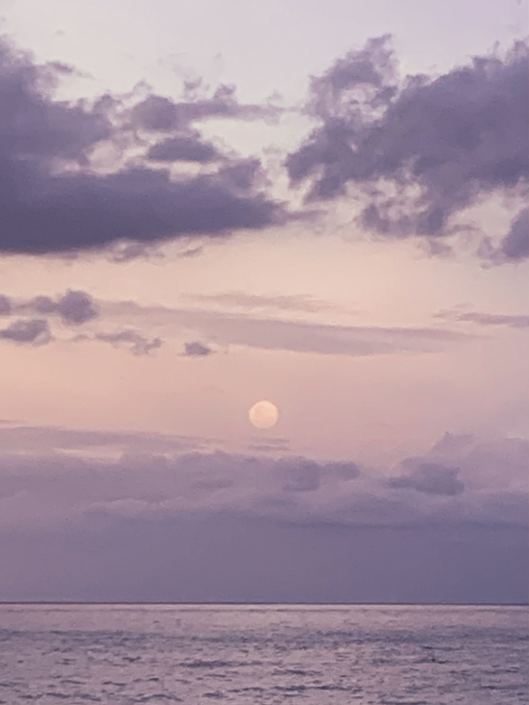 pretty blurry photo of the rising full moon over the sea, the hazy clouds and sea surface reflecting light and shadow in shades of lavender and peach