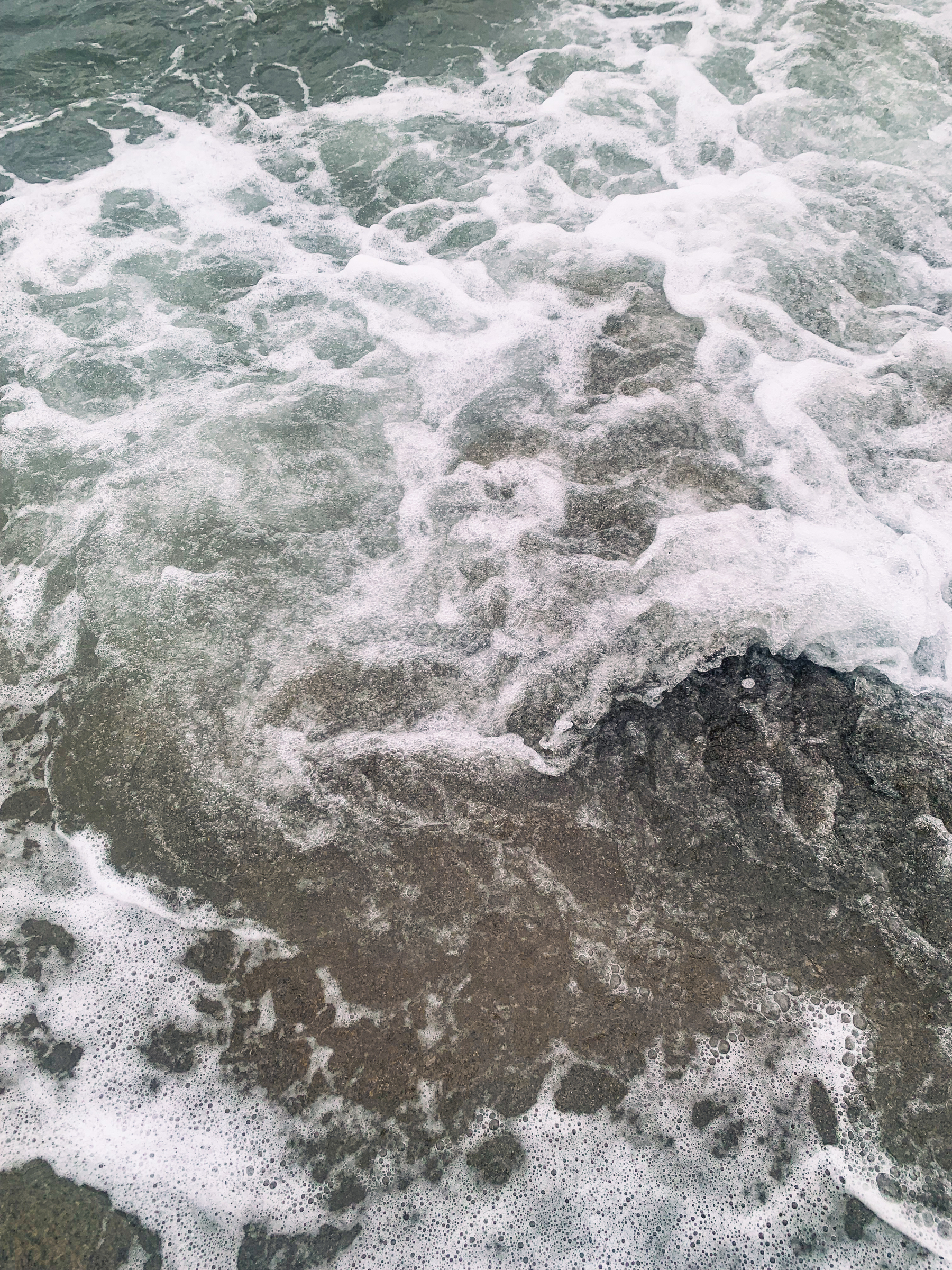 photo taken at the beach of a frothy swirl of greenish seawater over beige-brownish sand