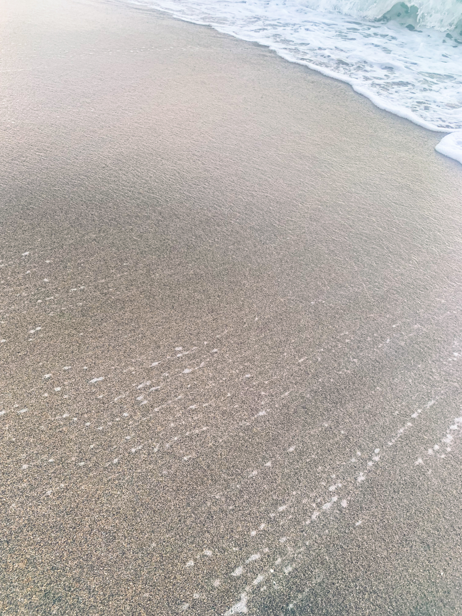 photo at the beach of water pulling away from sand almost out of the frame, into the upper right-hand corner of the image, suffused with luminescent golden-beige